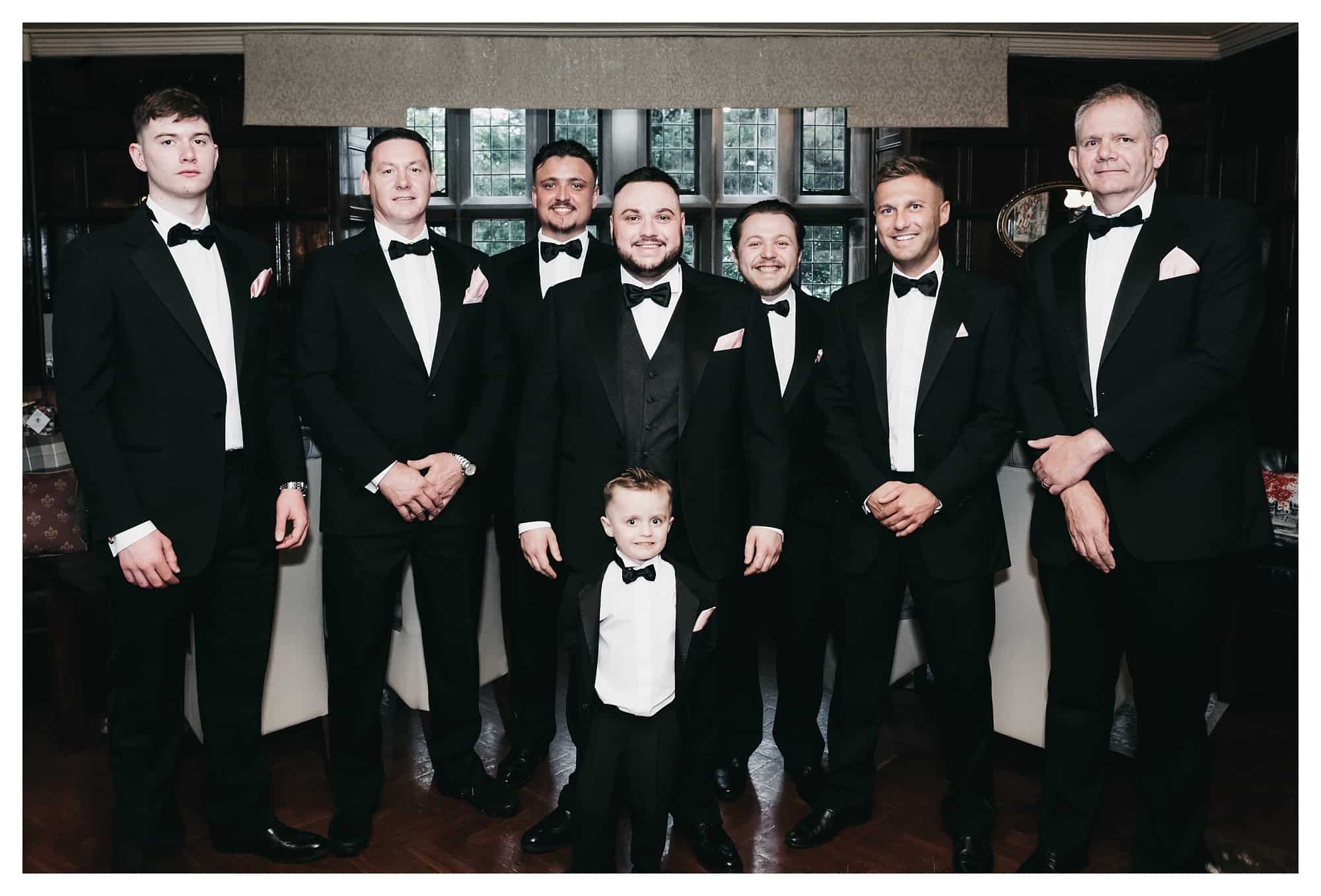 Group shot photograph of groomsmen wearing matching black tuxedos at inside the library at rogerthorpe manor