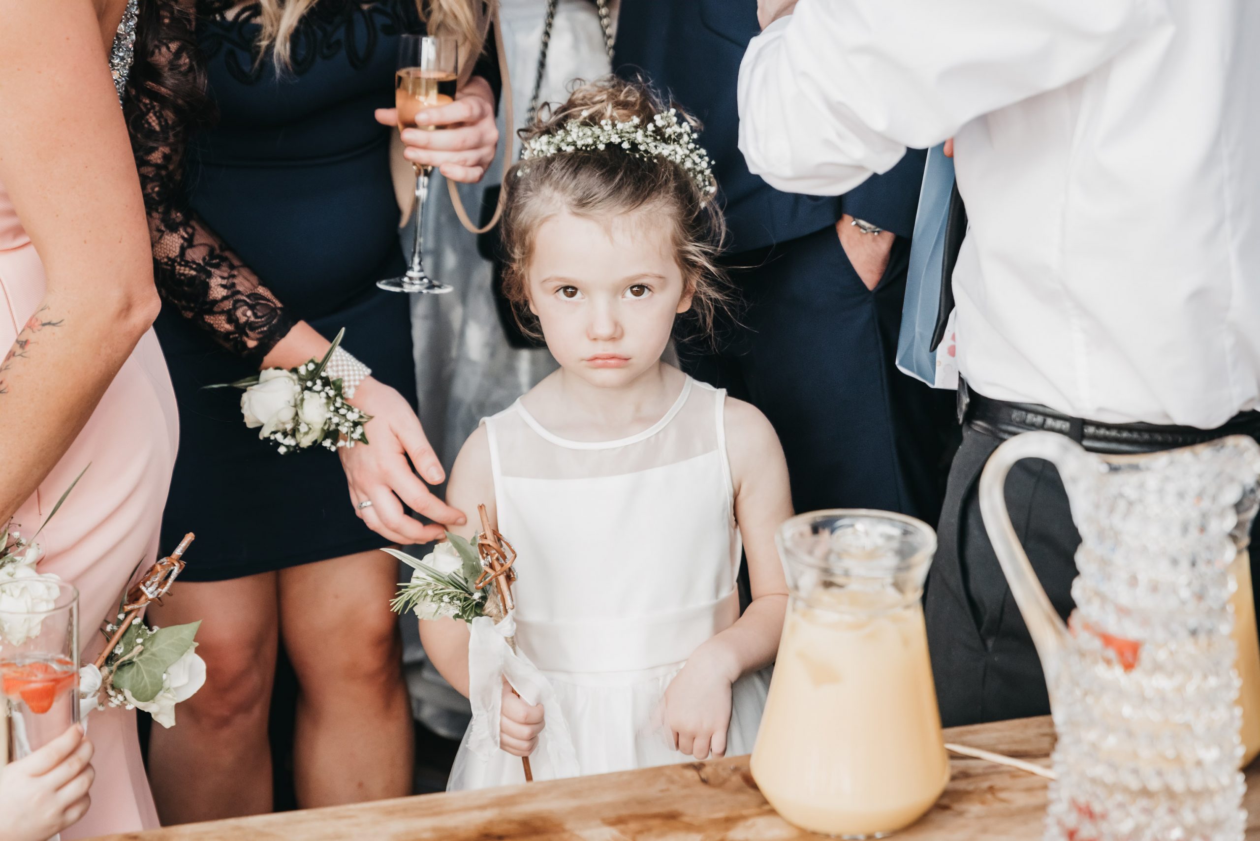 This image is of a little flower girl at a wedding looking directly into the camera, the expression on her face is one of been not happy