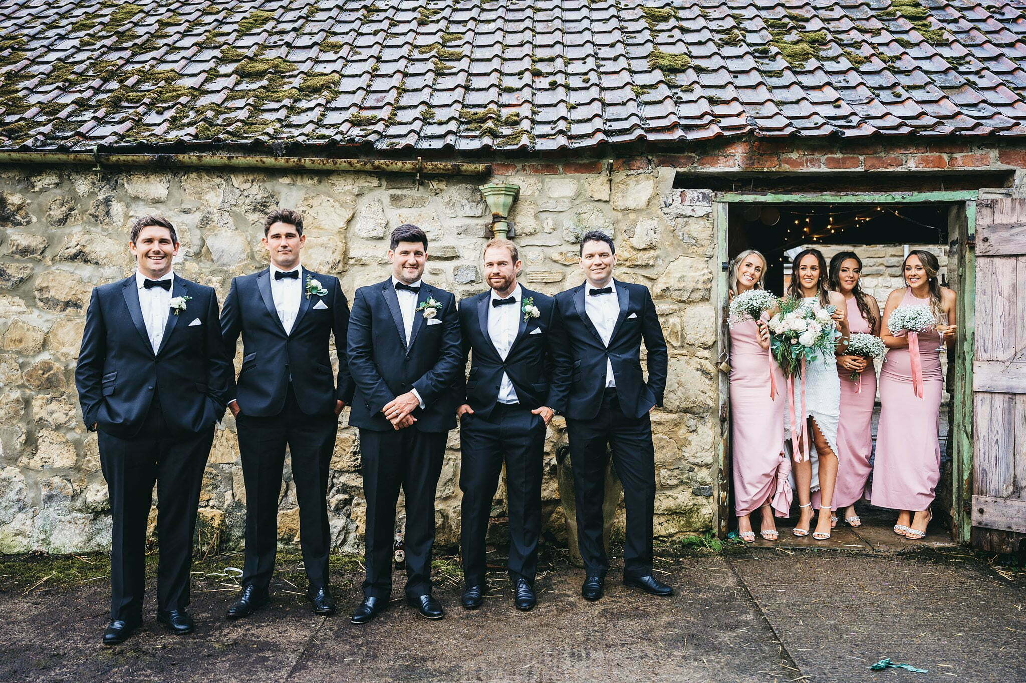 photograph of bridesmaids posing with bride and groomsmen with groom in barn doorway,Tadcaster Rustic Yurt Wedding, Rustic Yurt Wedding Photos, Tadcaster Wedding Photographer