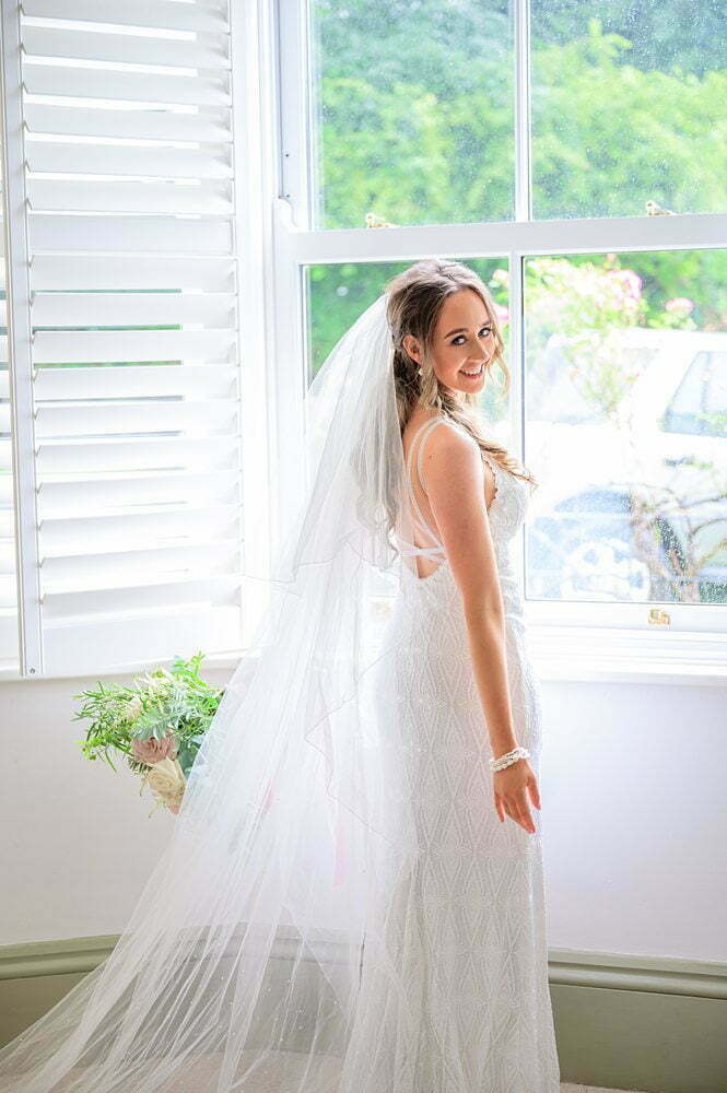 Photograph of bride posing with flowers in a wedding dress next to a window, Tadcaster Wedding Photographer