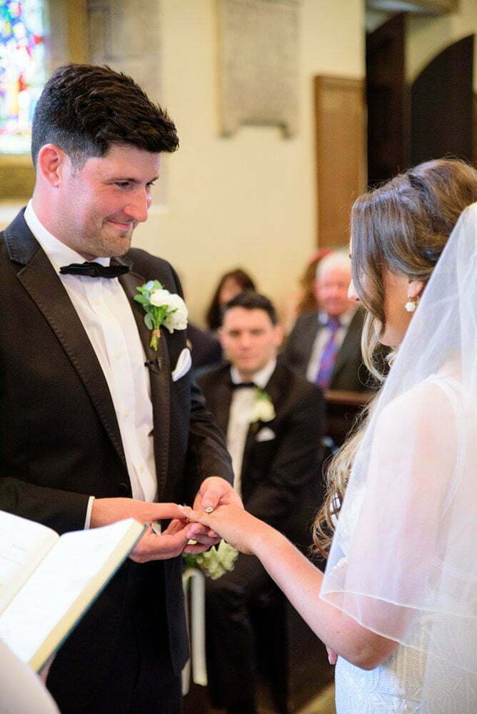 photograph of groom puting ring on brides finger at St Andrew Church, Newton Kym, Tadcaster Wedding Photographer