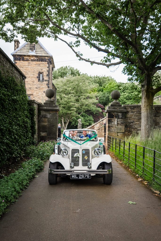 photo of wedding car with bride and groom smiling with shibden Hall in the background