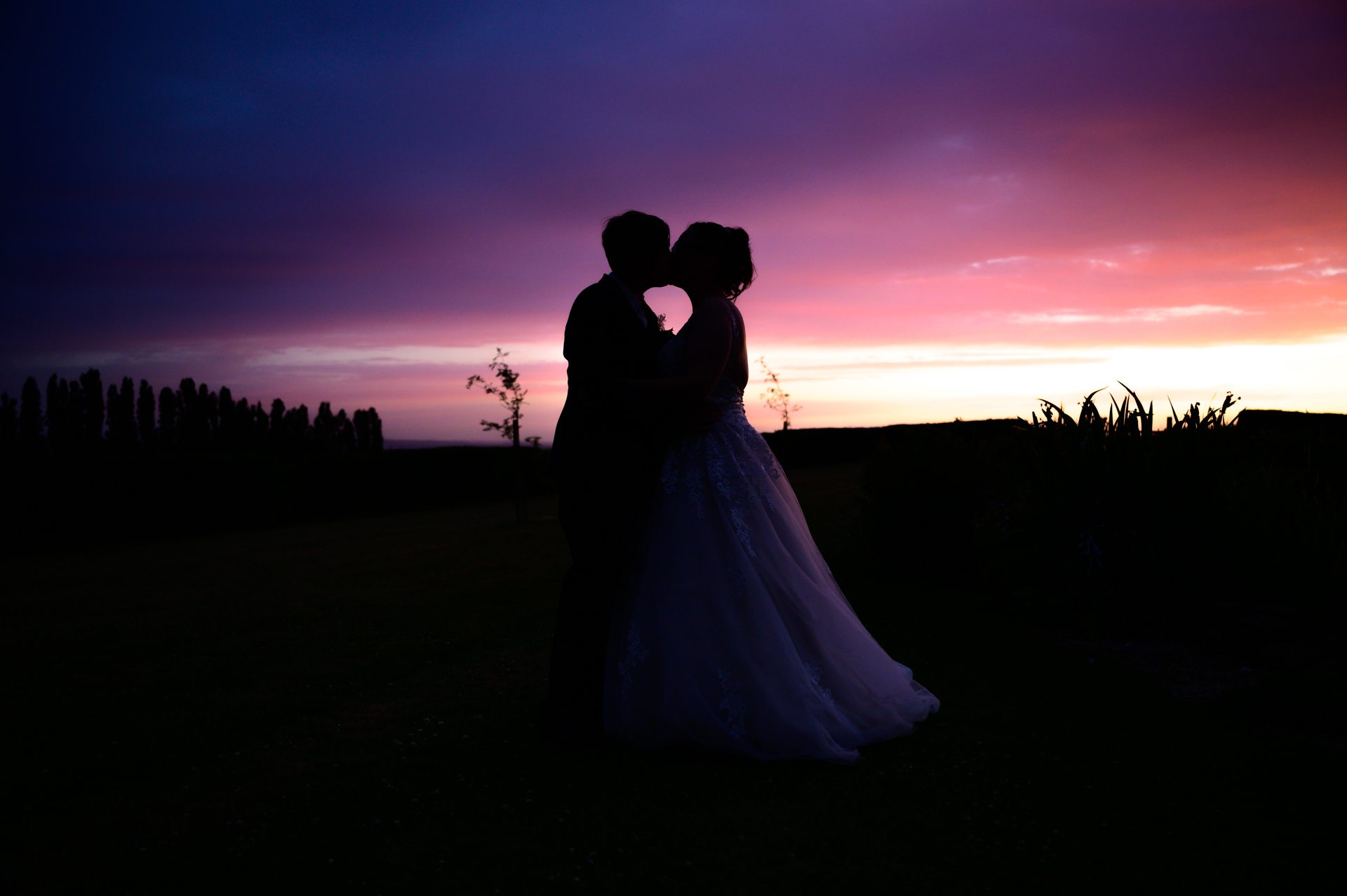 bride and bride kissing with sunset behind them , kings croft Hotel