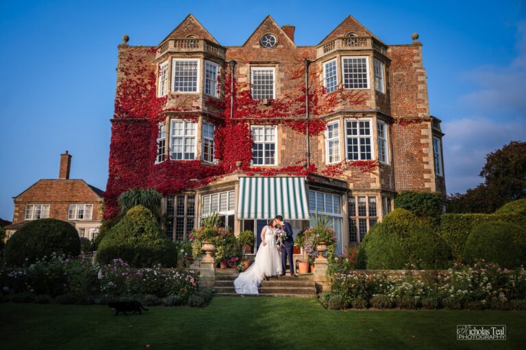 Bride and groom kiss on steps of Goldsborough Hall, North Yorkshire, with red ivy.