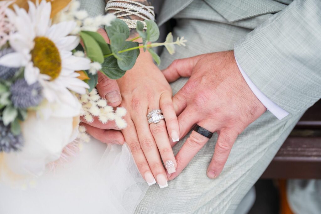 Close-up of bride and groom's hands with wedding rings, bouquet, and veil. Romantic, intimate.