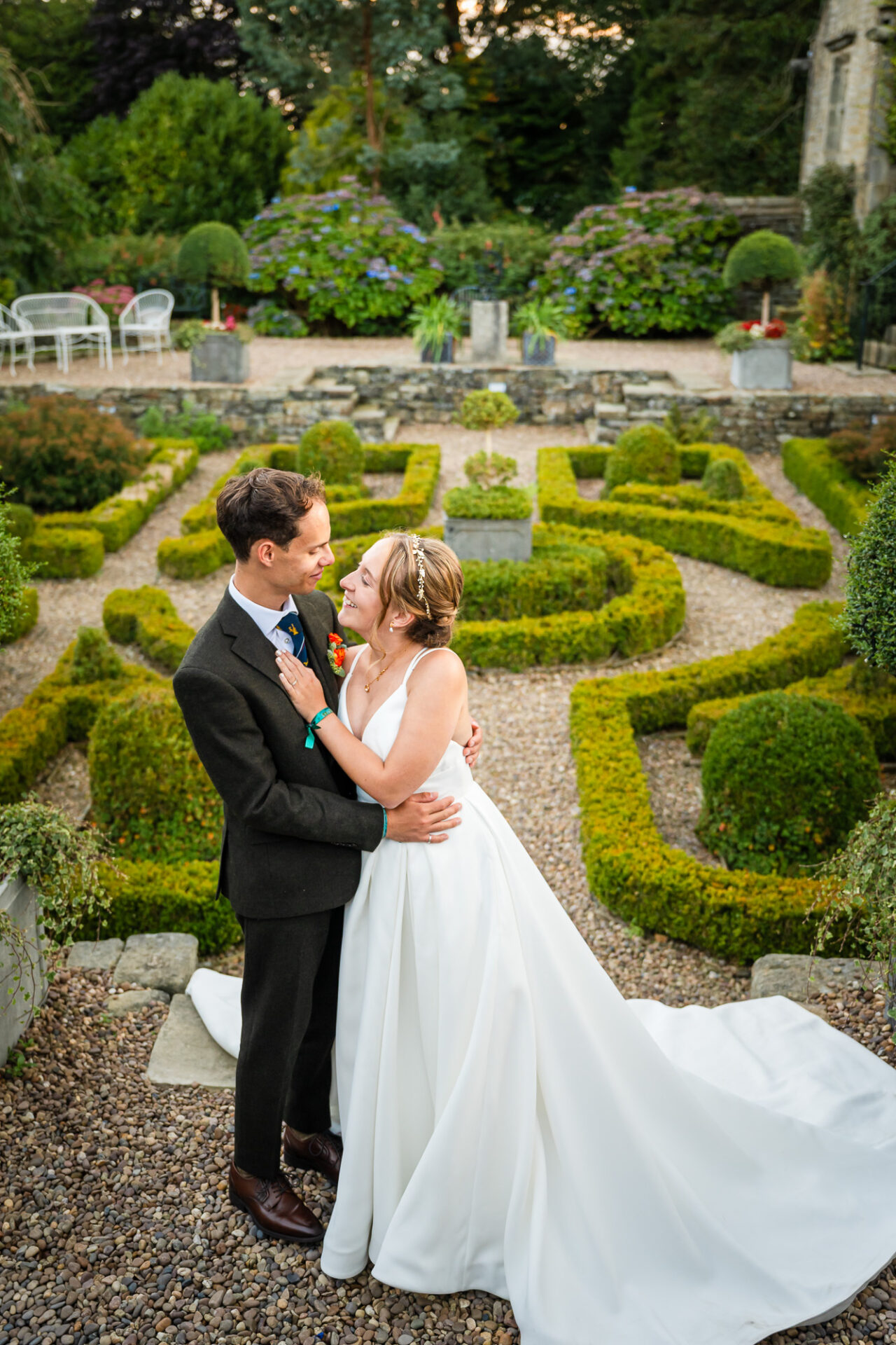 Bride & groom embrace in a formal garden, timeless wedding photography style.