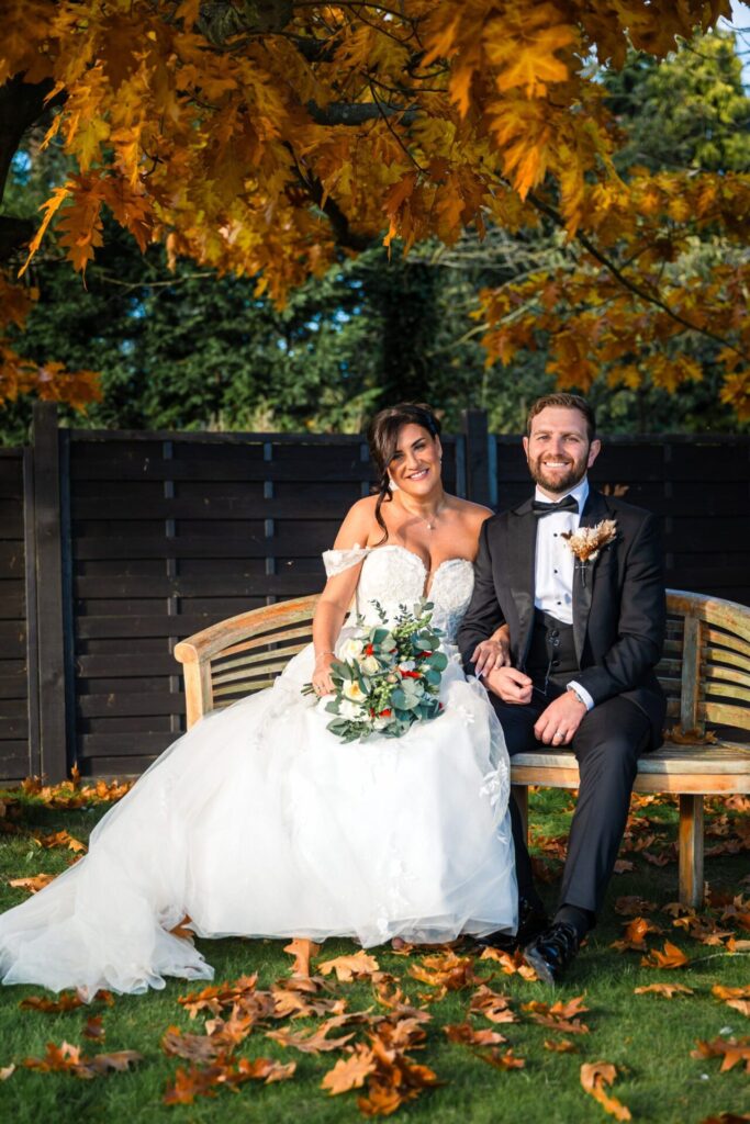 Bride and groom on bench, autumn leaves, Woodstock Weddings, editorial style.